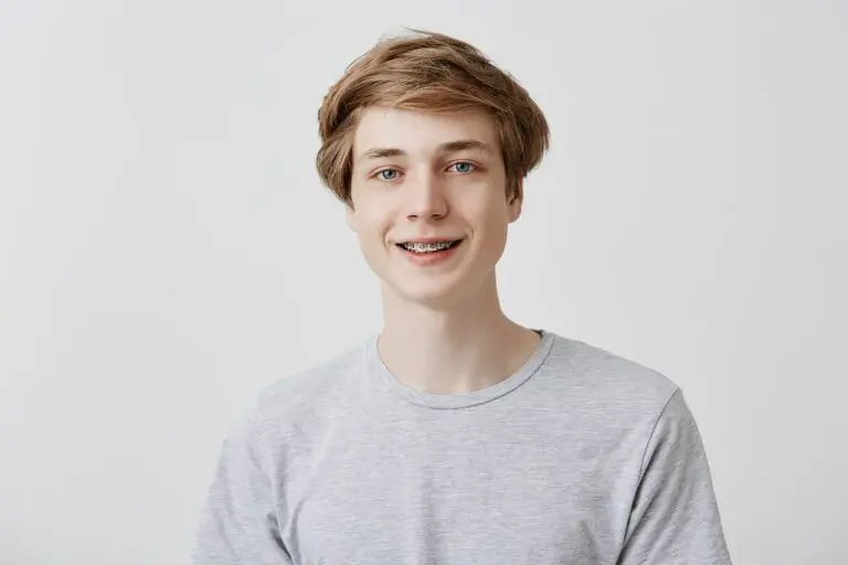 A teenage boy with light brown hair and braces, wearing a light gray t-shirt, smiles in front of a plain white background at Levine Orthodontics in Fort Myers, Cape Coral or Lehigh Acres, FL.
