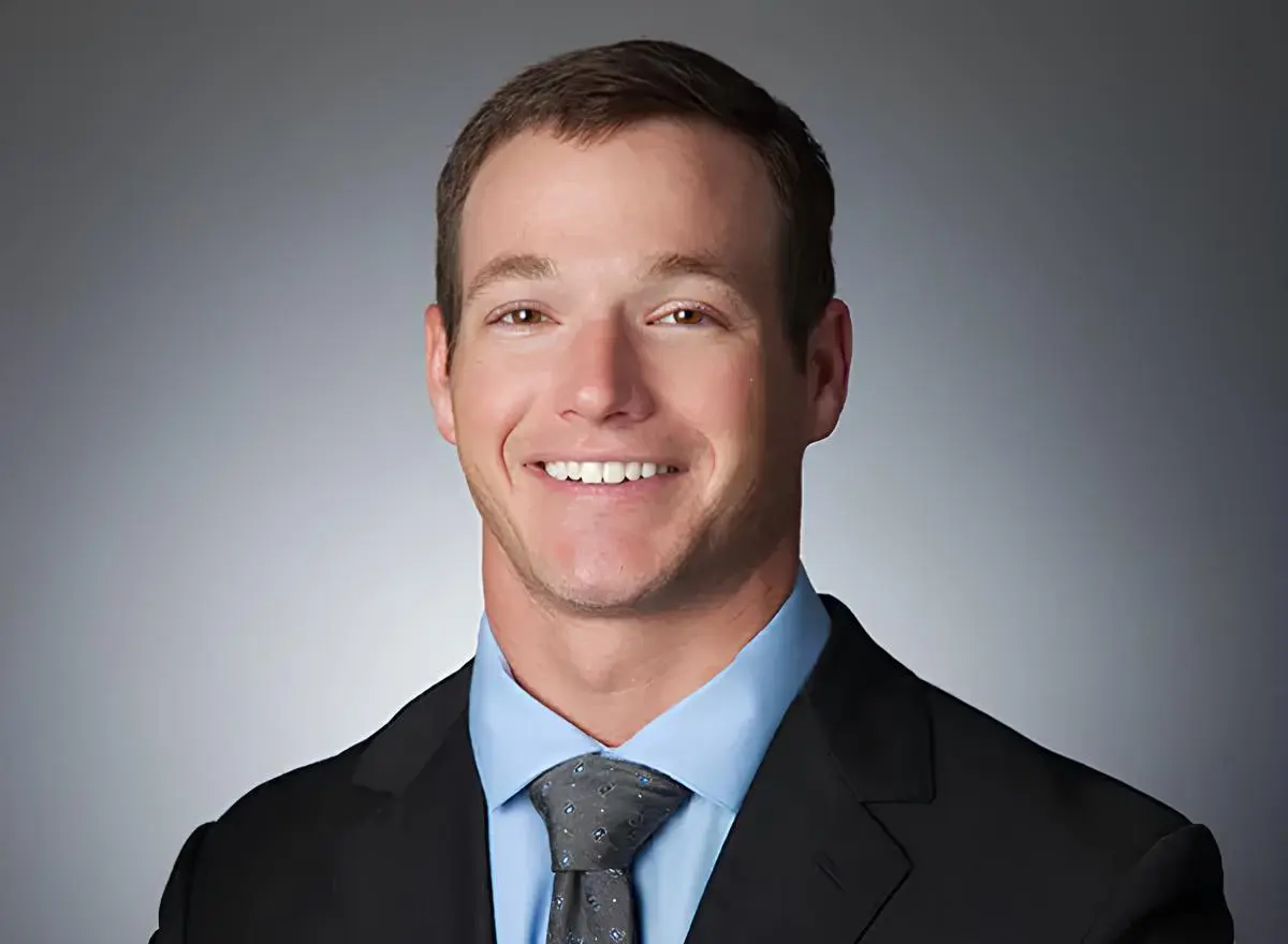 At Levine Orthodontics in Lehigh Acres, FL, Dr. Alex Levine—recognized by his short brown hair and friendly smile—is pictured against a plain gray background wearing a dark suit, light blue shirt and patterned tie.