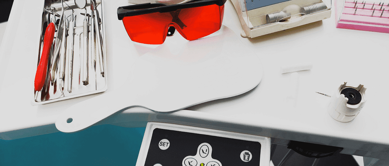 On a white surface at Levine Orthodontics in Fort Myers, Cape Coral or Lehigh Acres, FL, dental tray tools—including metal braces instruments, a handheld mirror, red safety glasses and equipment controls—are displayed.