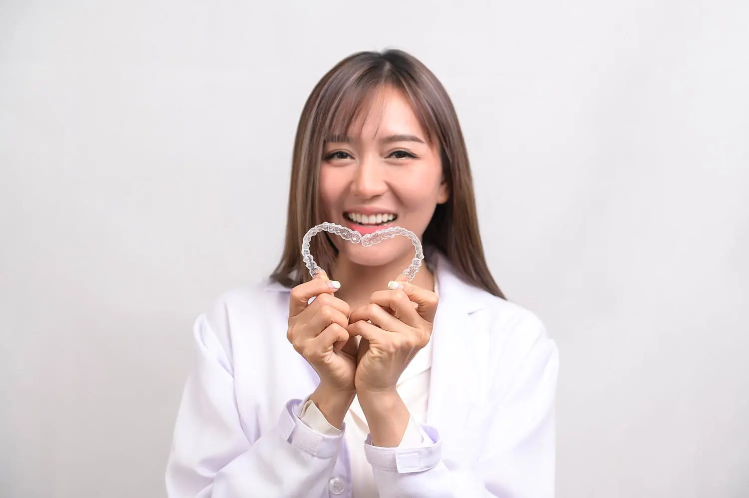 At Levine Orthodontics in Fort Myers, Cape Coral or Lehigh Acres, FL, a professional in a white coat warmly presents two clear aligners shaped into a heart, embodying the innovative care that makes Invisalign's payment plan accessible for anyone desiring a radiant smile.