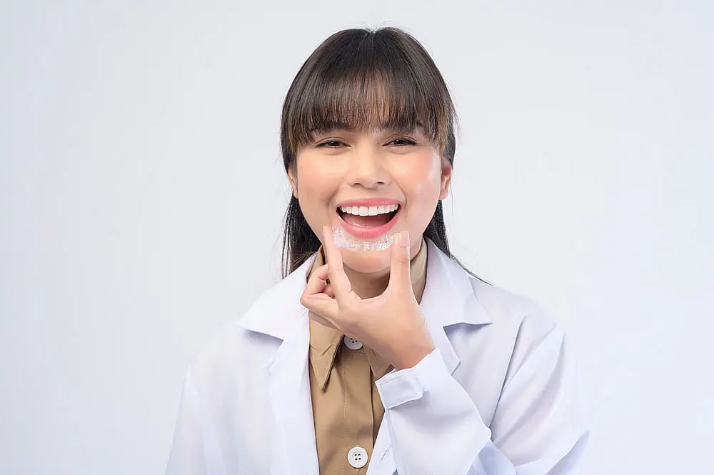 A person in a white coat warmly displays Invisalign® Clear Aligners against a plain background, highlighting Levine Orthodontics available in Cape Coral, FL.