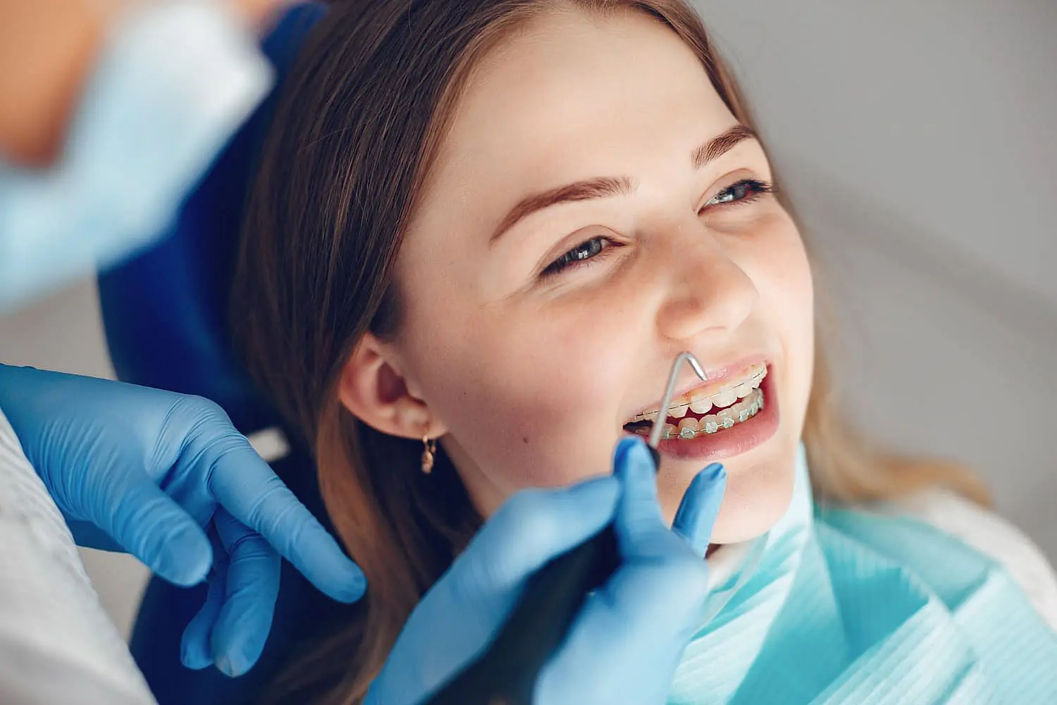 At Levine Orthodontics in Cape Coral FL, a dentist in blue gloves examines a young woman with clear braces during her dental checkup.