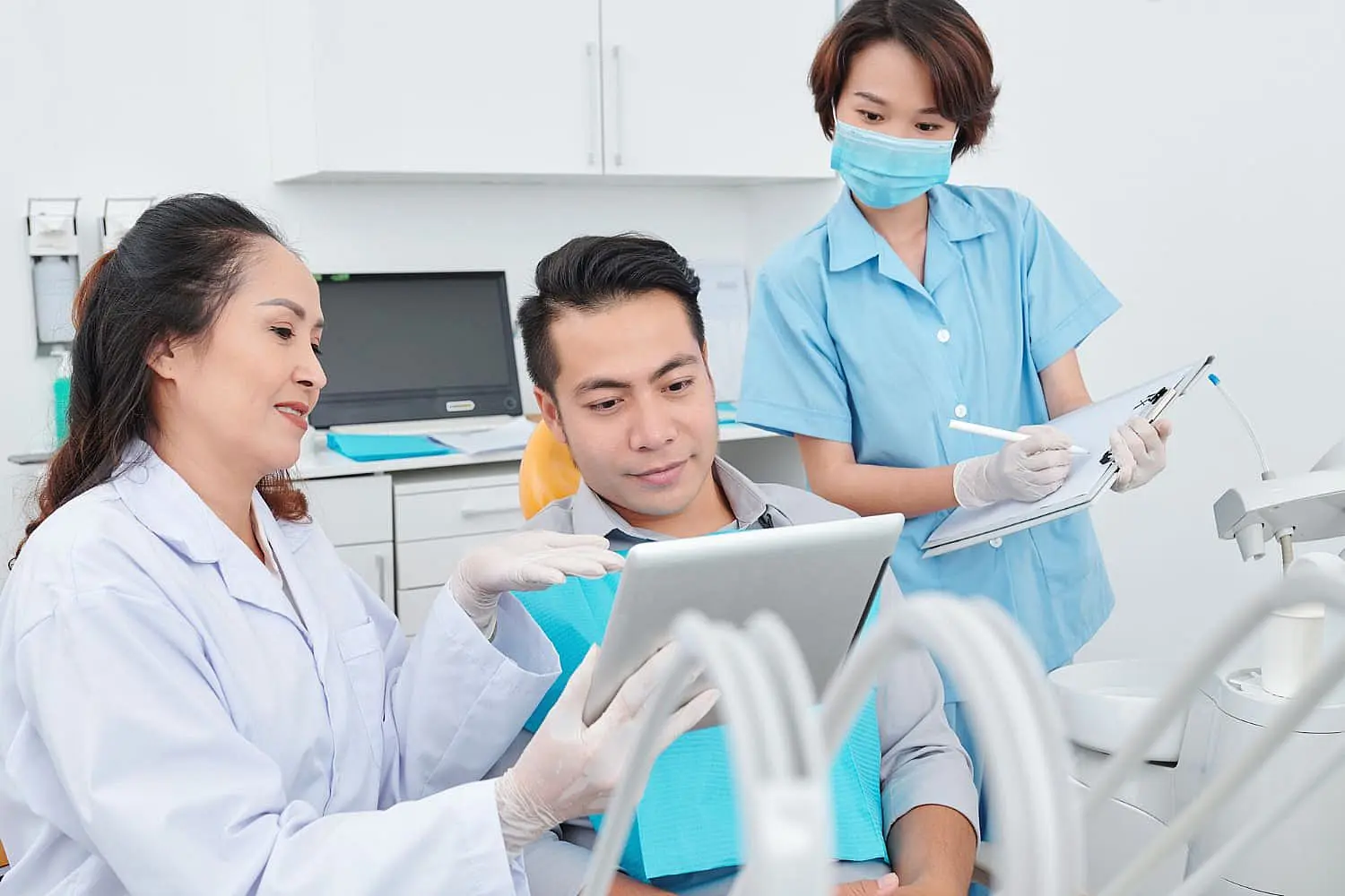 At Levine Orthodontics in Fort Myers, Cape Coral or Lehigh Acres, FL, two dental professionals discuss adult orthodontics with a patient, sharing information on a tablet while another team member takes notes in the clinic.