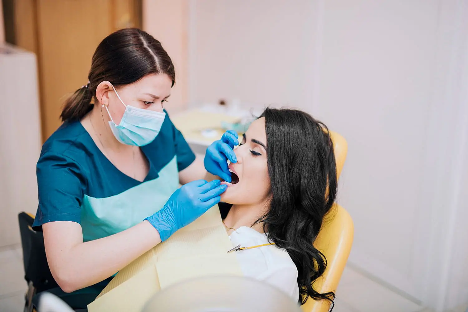 In a modern dental office, a professional at Levine Orthodontics in Fort Myers, Cape Coral or Lehigh Acres, FL, examines a patient's teeth for signs of tongue thrust while wearing gloves and a mask.