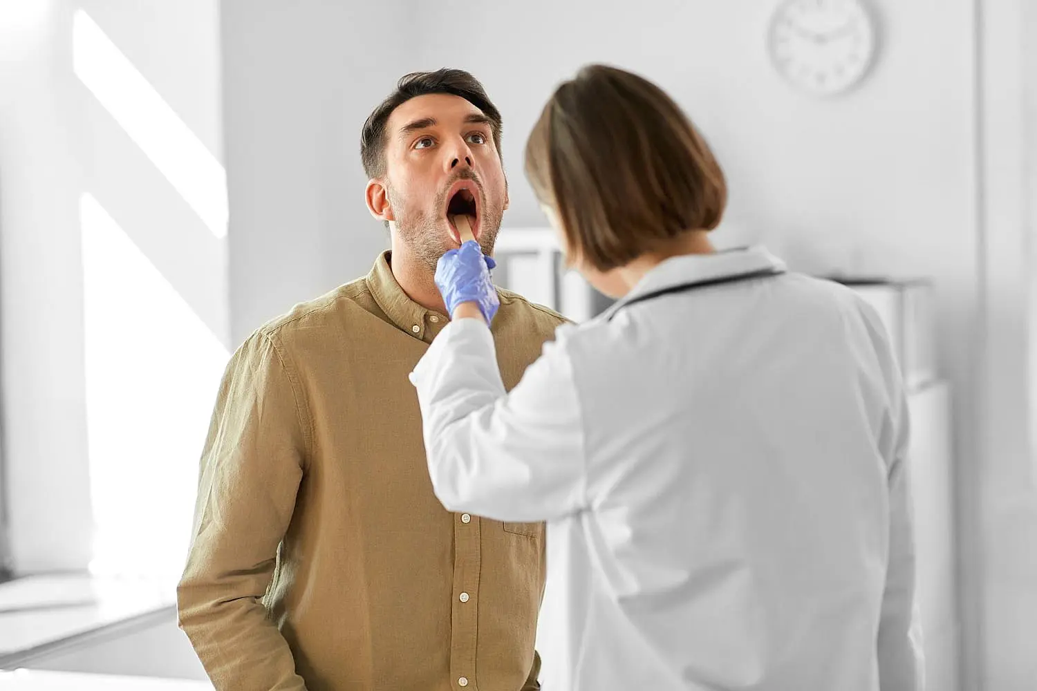 The doctor at Levine Orthodontics in Fort Myers, Cape Coral or Lehigh Acres, FL, meticulously checks the patient's throat for tongue thrust signs using a tongue depressor.