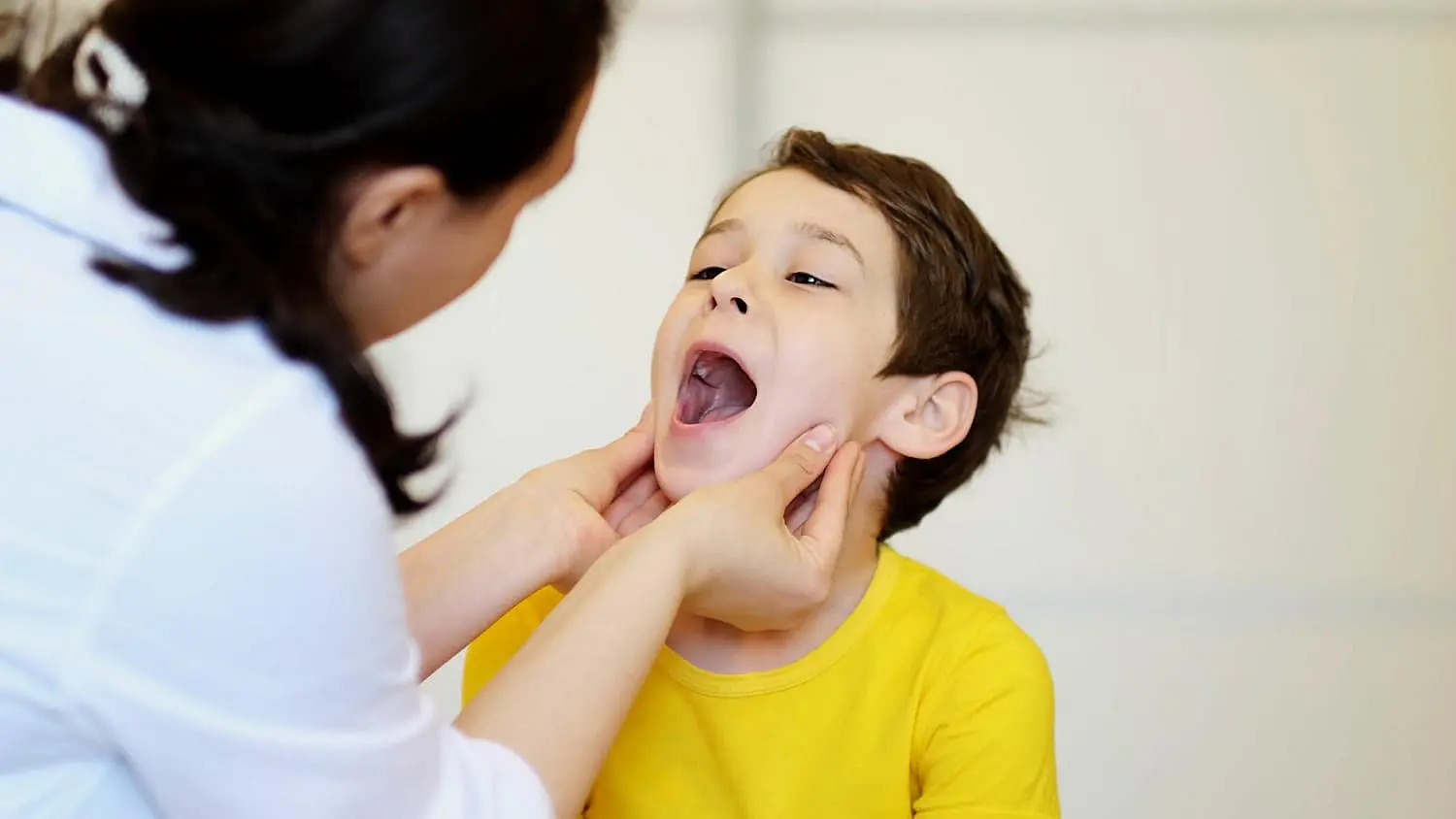 A gentle oral health check, like an initial evaluation by a children’s orthodontist at Levine Orthodontics in Fort Myers, Cape Coral or Lehigh Acres, FL, is shown as an adult examines a young boy’s open mouth.