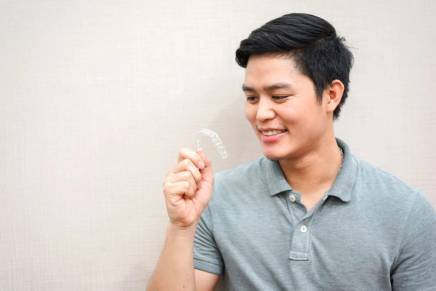 A man in a gray polo shirt examines Invisalign® Clear Aligners against a plain, light background at Levine Orthodontics in Cape Coral, FL.