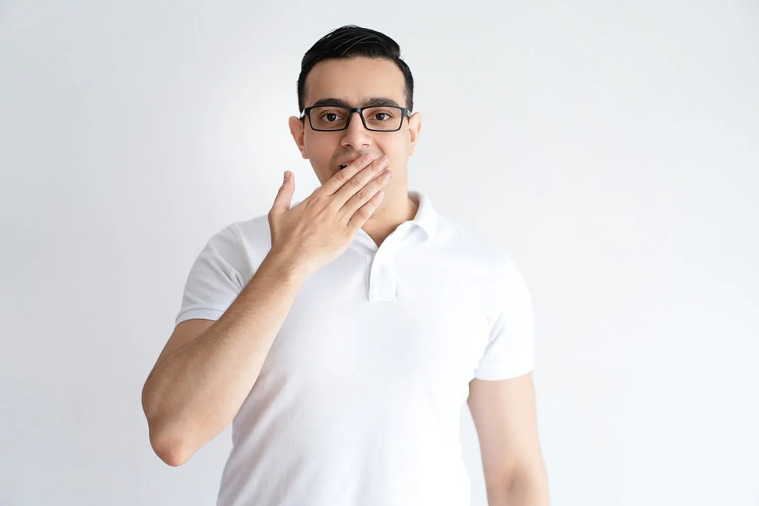 Against a plain white background, a man in a white shirt and glasses discreetly covers his mouth, possibly to avoid revealing any mouth breathing. If you're experiencing similar concerns in Fort Myers, Cape Coral or Lehigh Acres, FL, Levine Orthodontics can help.