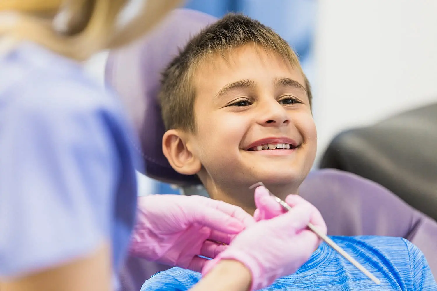 At Levine Orthodontics in Fort Myers, Cape Coral or Lehigh Acres, FL, a young boy smiles in a dental chair while a children’s orthodontist with pink gloves prepares to examine his teeth.
