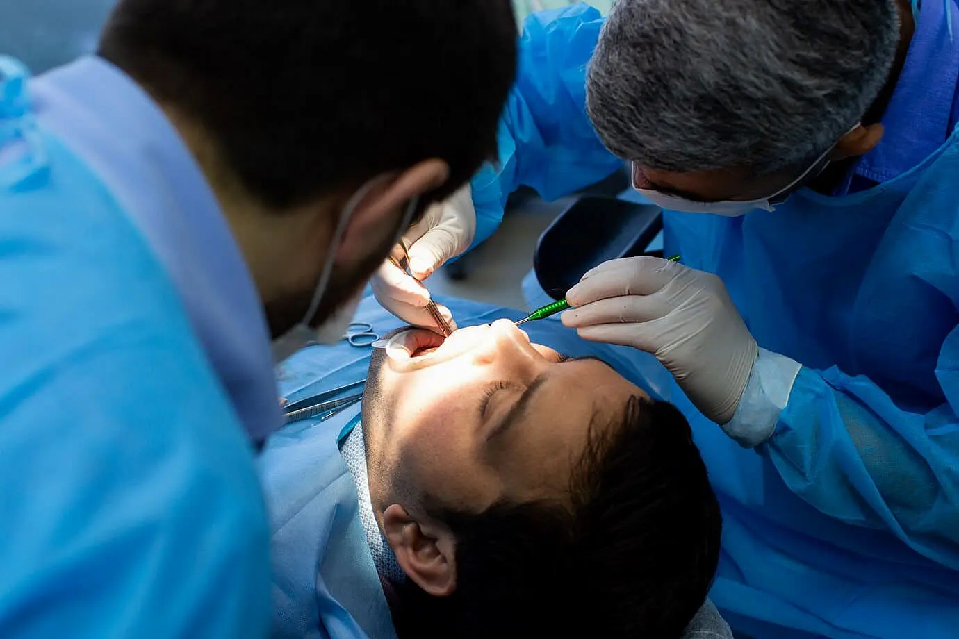 At Levine Orthodontics in Fort Myers, Cape Coral or Lehigh Acres FL, a dentist and assistant, both in blue protective gowns and gloves, examine a patient's mouth for signs of tongue thrust as the patient lies in a dental chair.