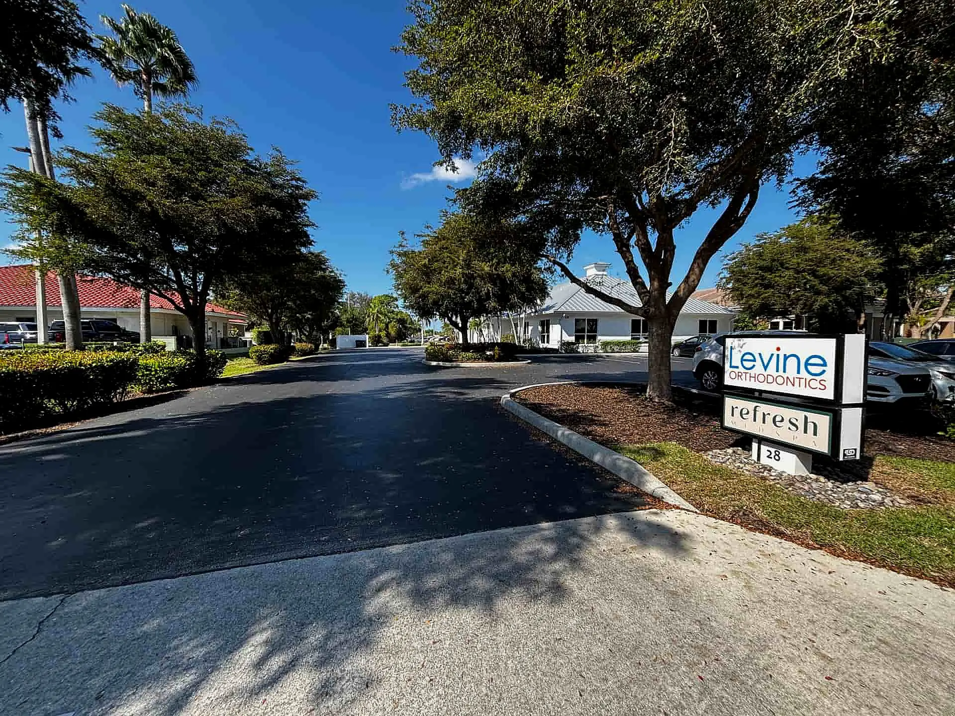 On a sunny day, Levine Orthodontics in Fort Myers, Cape Coral or Lehigh Acres, FL is recognizable by its "refresh" sign amidst trees and parked cars. Inside, you can find detailed information about affordable braces costs to help you smile confidently.