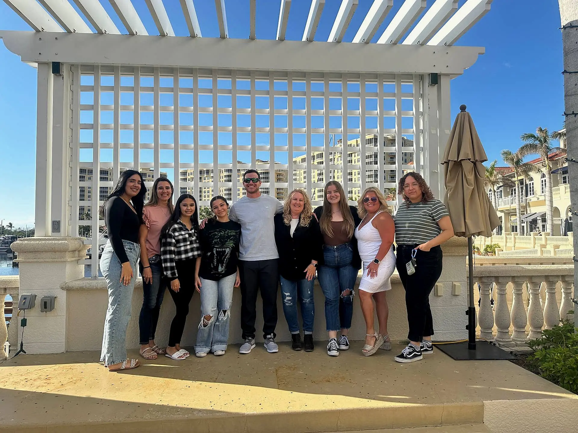 Under a pergola with buildings and a clear sky in the background, a team of adult orthodontics experts, consisting of eight women and one man, represents Levine Orthodontics in Fort Myers, Cape Coral or Lehigh Acres, FL.