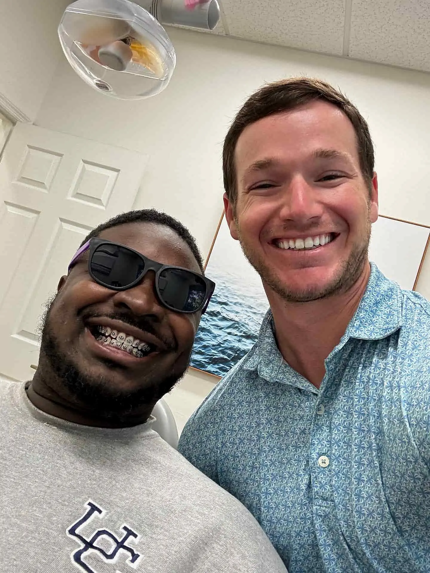 At Levine Orthodontics in Lehigh Acres FL, two men pose for a photo at Dr. Alex Levine's office—one wearing braces, sunglasses, and a sweatshirt; the other in a patterned shirt.