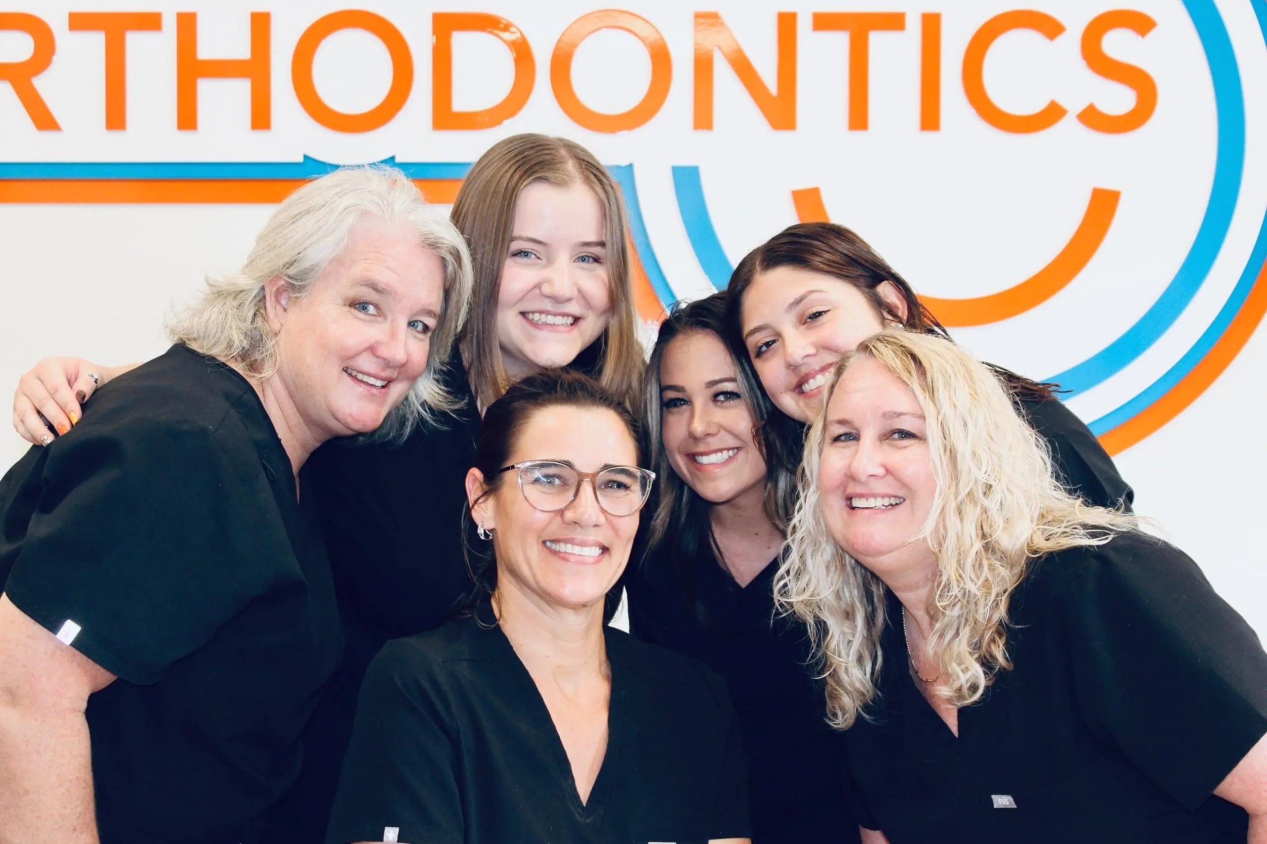 In Fort Myers, Cape Coral or Lehigh Acres, FL, six smiling women in black uniforms represent the welcoming spirit of a children's orthodontist as they pose together in front of a Levine Orthodontics sign.