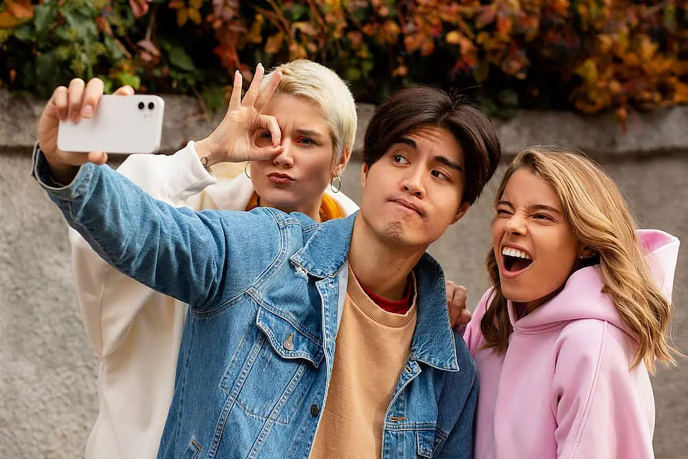 In a joyful outdoor selfie, three friends in casual wear capture the moment. One skillfully holds the phone, another adds flair with a playful hand gesture and the third grins widely, showcasing gleaming teeth improved by discreet braces from Levine Orthodontics in Fort Myers, Cape Coral or Lehigh Acres, FL.