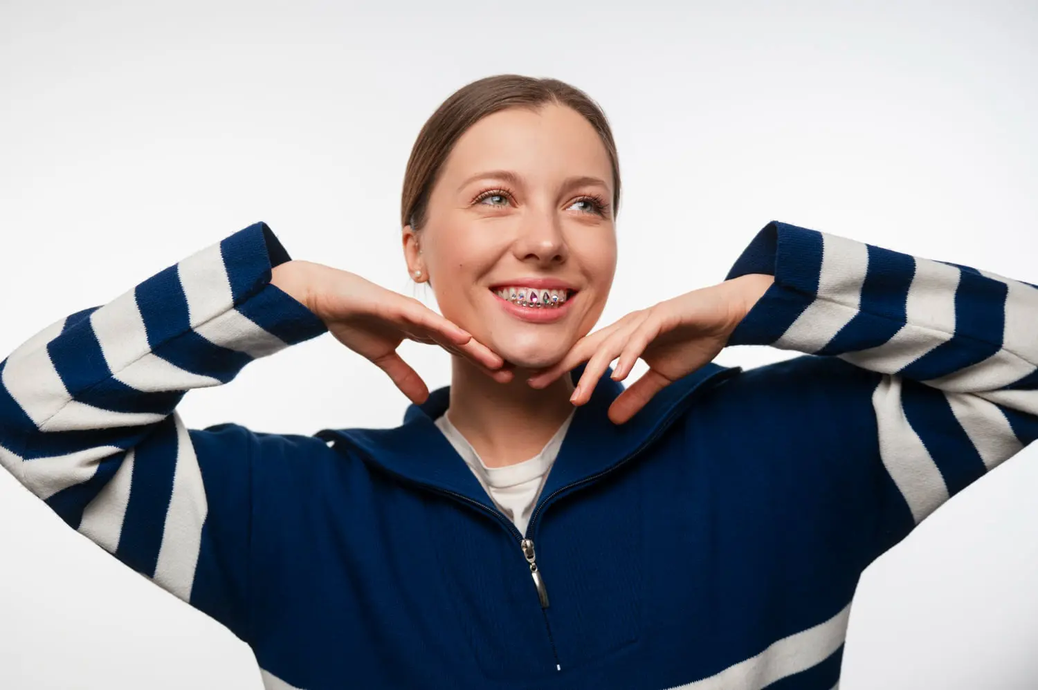 A young woman in a blue and white striped sweater, smiling with metal braces, poses against a plain white background at Levine Orthodontics in Fort Myers, Cape Coral or Lehigh Acres, FL.