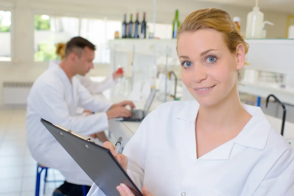At Levine Orthodontics, a woman in a white lab coat holds a clipboard and pen while reviewing plan limitations for orthodontic insurance plans, with another person working in the background. This scene takes place in Fort Myers, Cape Coral, or Lehigh Acres, FL.