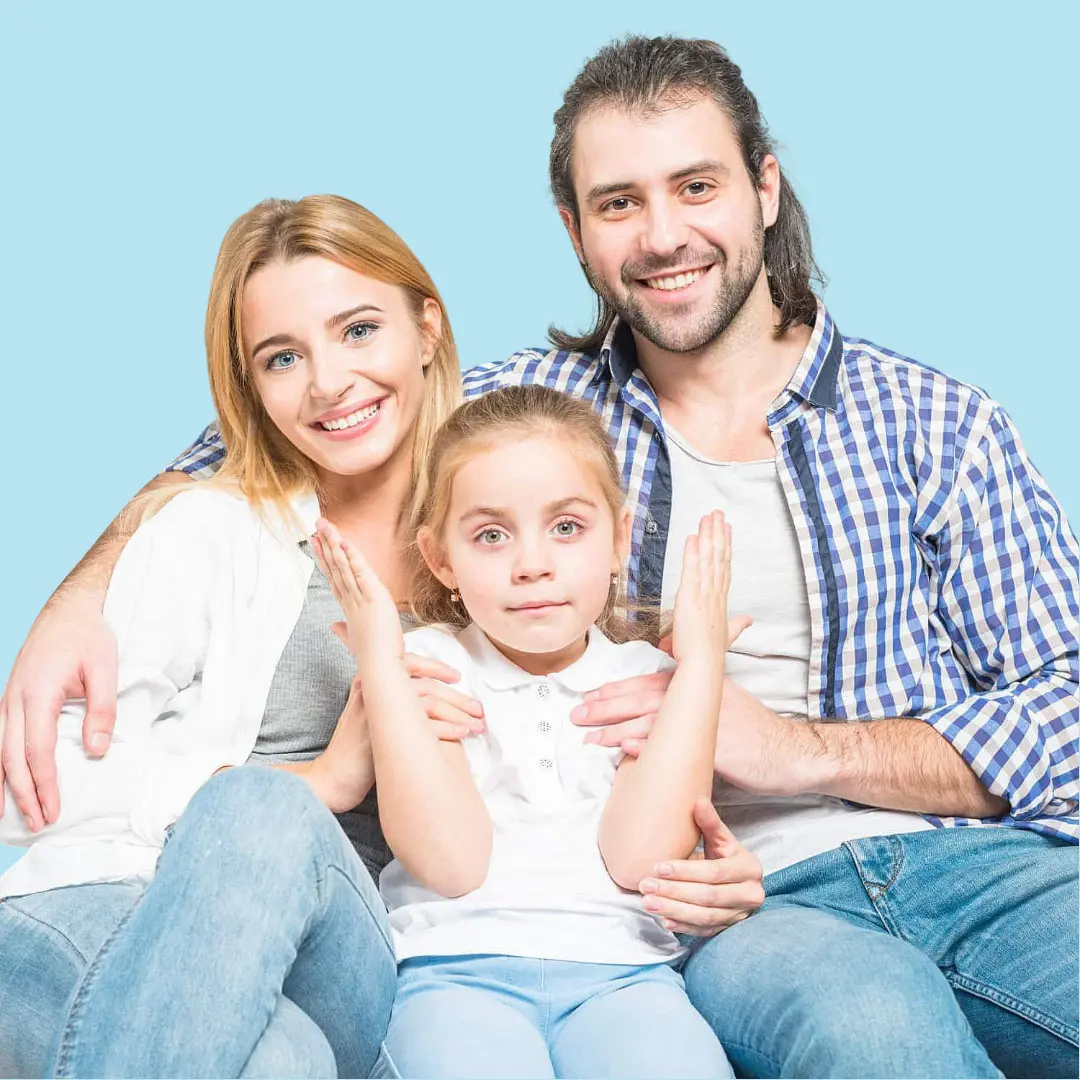 In a light blue setting, a man and woman sit closely, smiling at the camera while a young girl in front raises her hands with a neutral, confident expression demonstrating the results achieved with orthodontic appliances from Levine Orthodontics in Lehigh Acres, FL.
