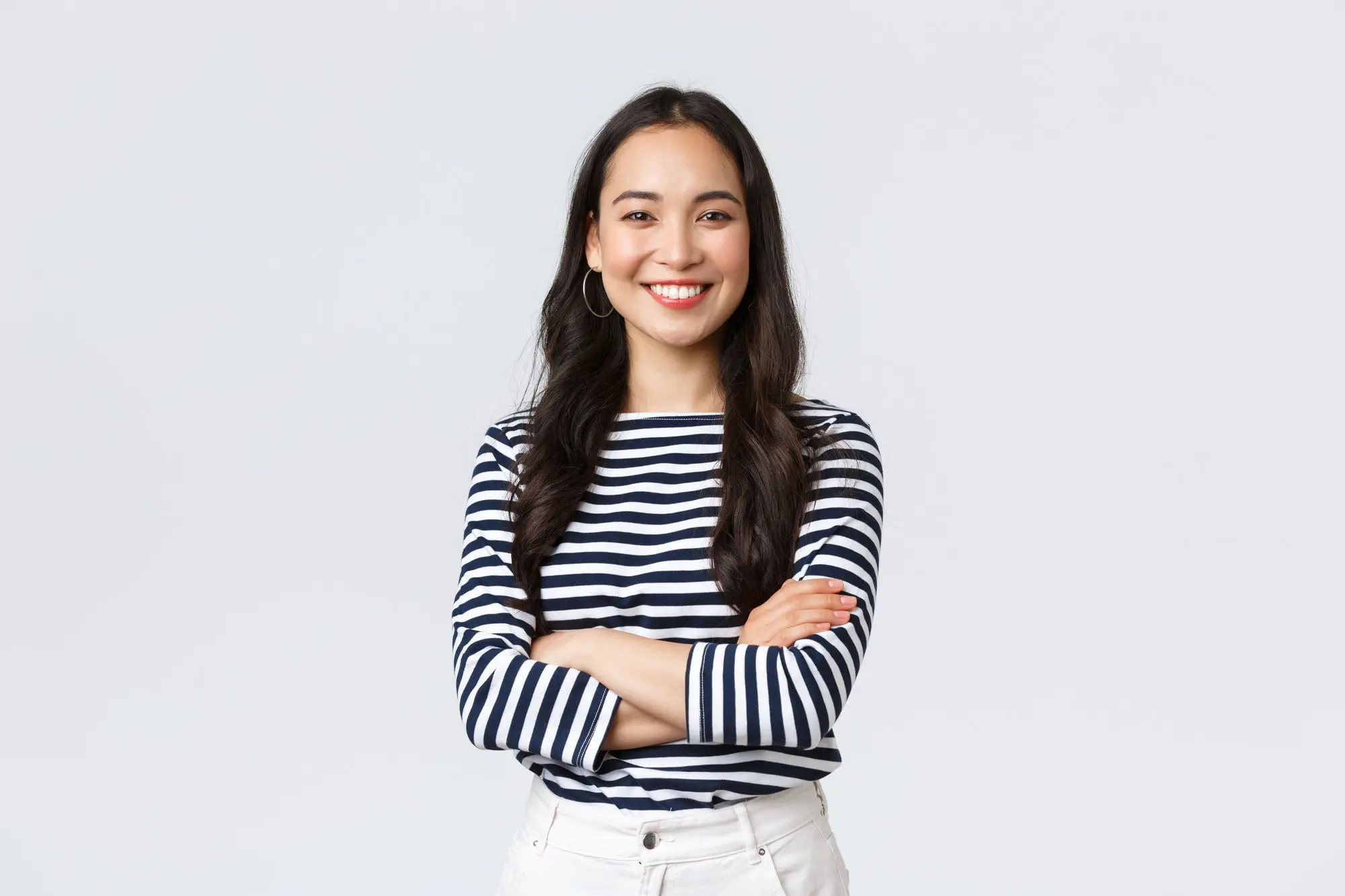 A woman with long dark hair, dressed in a black and white striped shirt and white pants, stands confidently with arms crossed and a smile—reflecting her satisfaction in choosing Levine Orthodontics for orthodontic insurance plans in Fort Myers, Cape Coral or Lehigh Acres, FL.