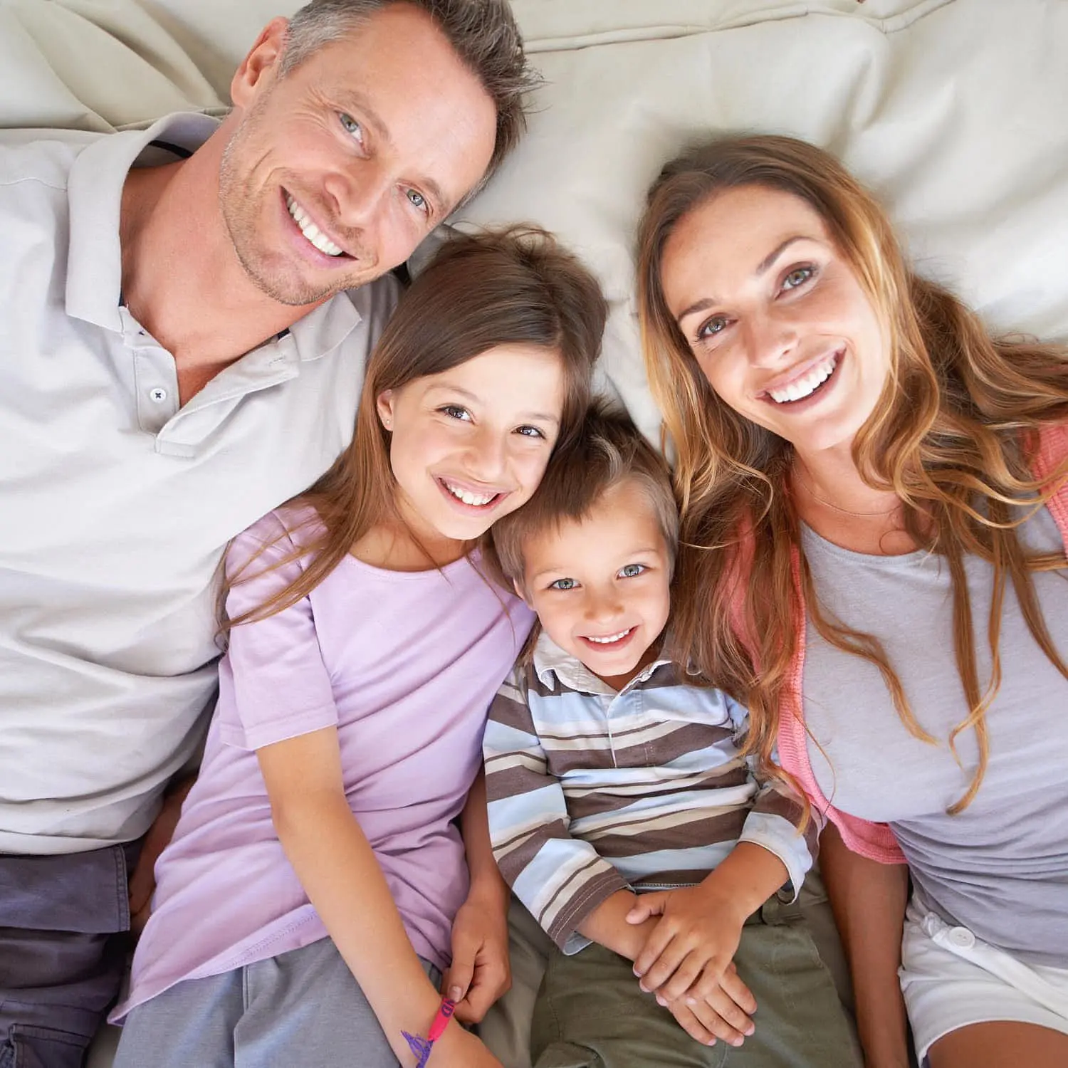 A man, woman, girl, and boy smile as they lie together on a couch, looking up at the camera—a joyful moment for Levine Orthodontics patients in Fort Myers, Cape Coral or Lehigh Acres, FL.
