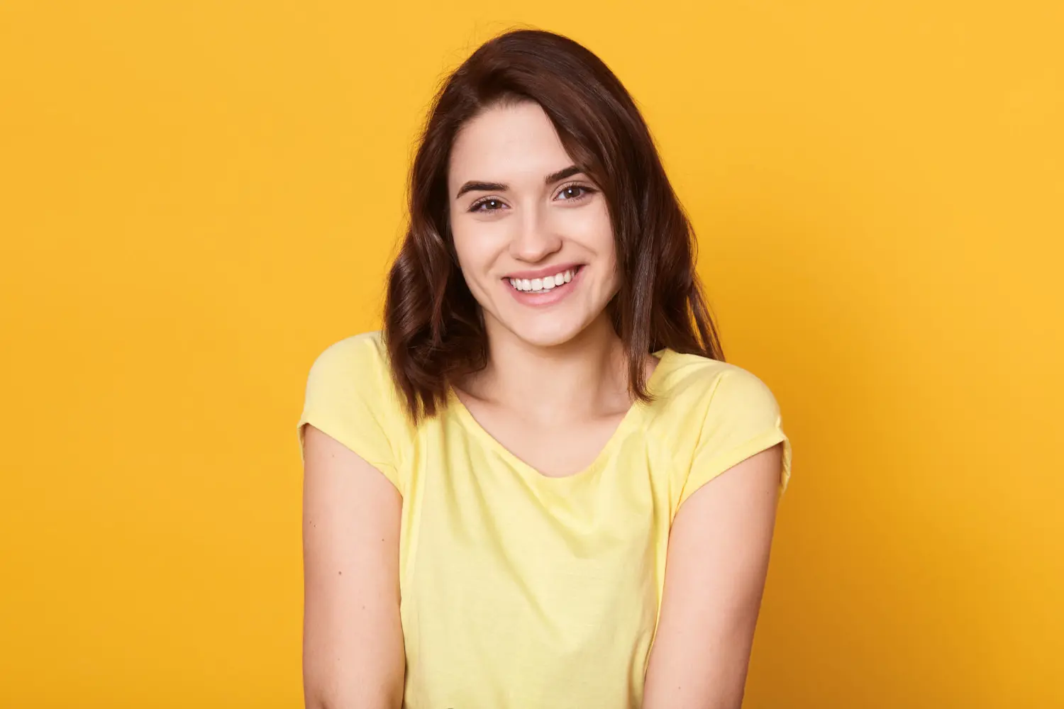 A young woman with brown hair and a yellow t-shirt confidently smiles, showing her adult braces—just one of the many happy patients at Levine Orthodontics in Fort Myers, Cape Coral, or Lehigh Acres, FL.