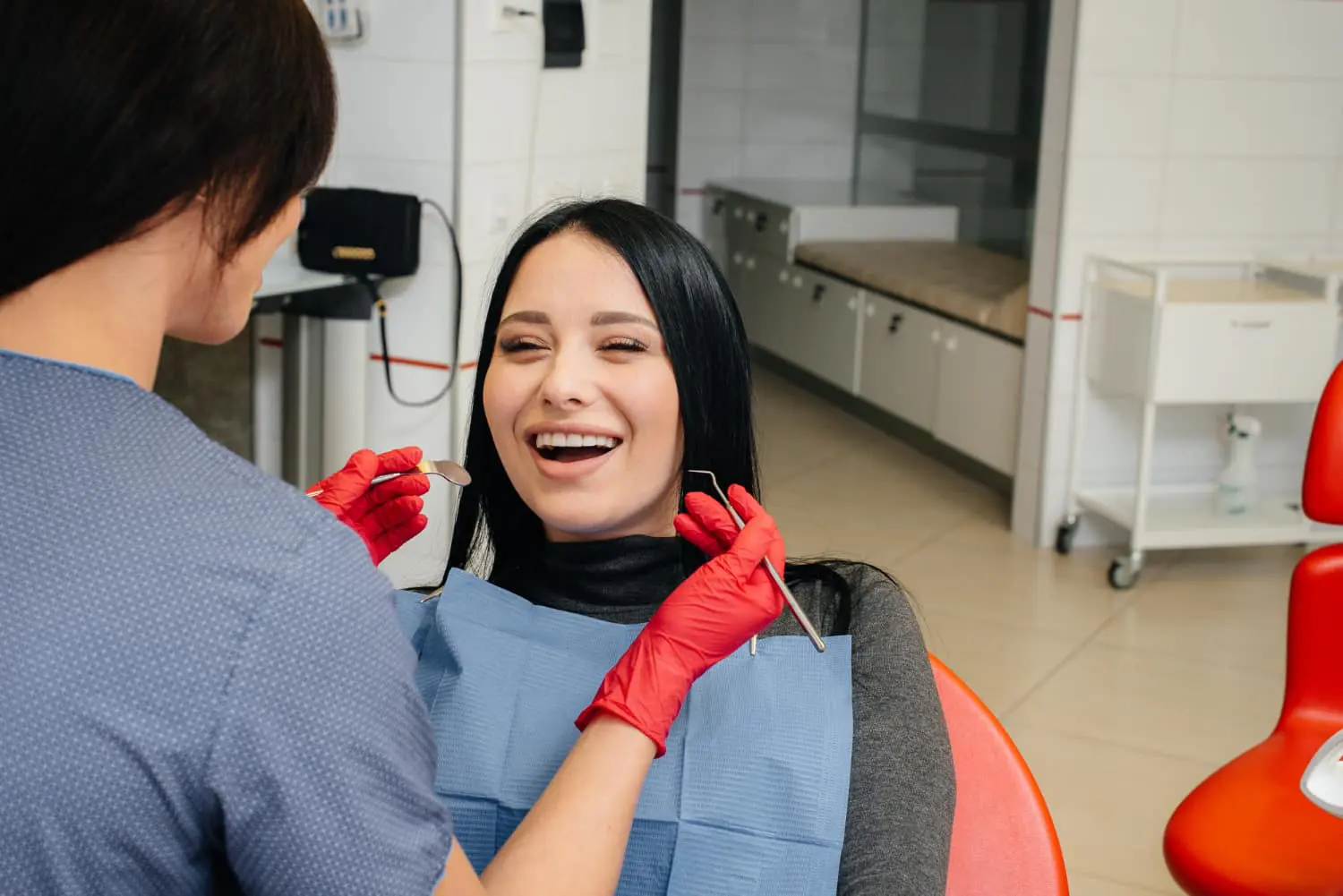At Levine Orthodontics in Fort Myers, Cape Coral, or Lehigh Acres, FL, a woman smiles in the dental chair while a professional with red gloves discusses Invisalign insurance coverage in a bright clinic.