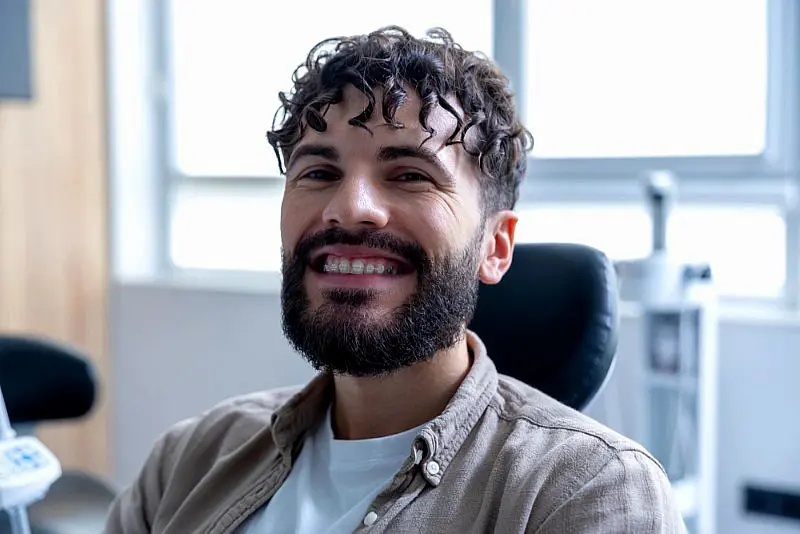 At Levine Orthodontics in Lehigh Acres FL, a man with curly hair and a beard smiles confidently in a dental chair, proudly displaying his clear braces.