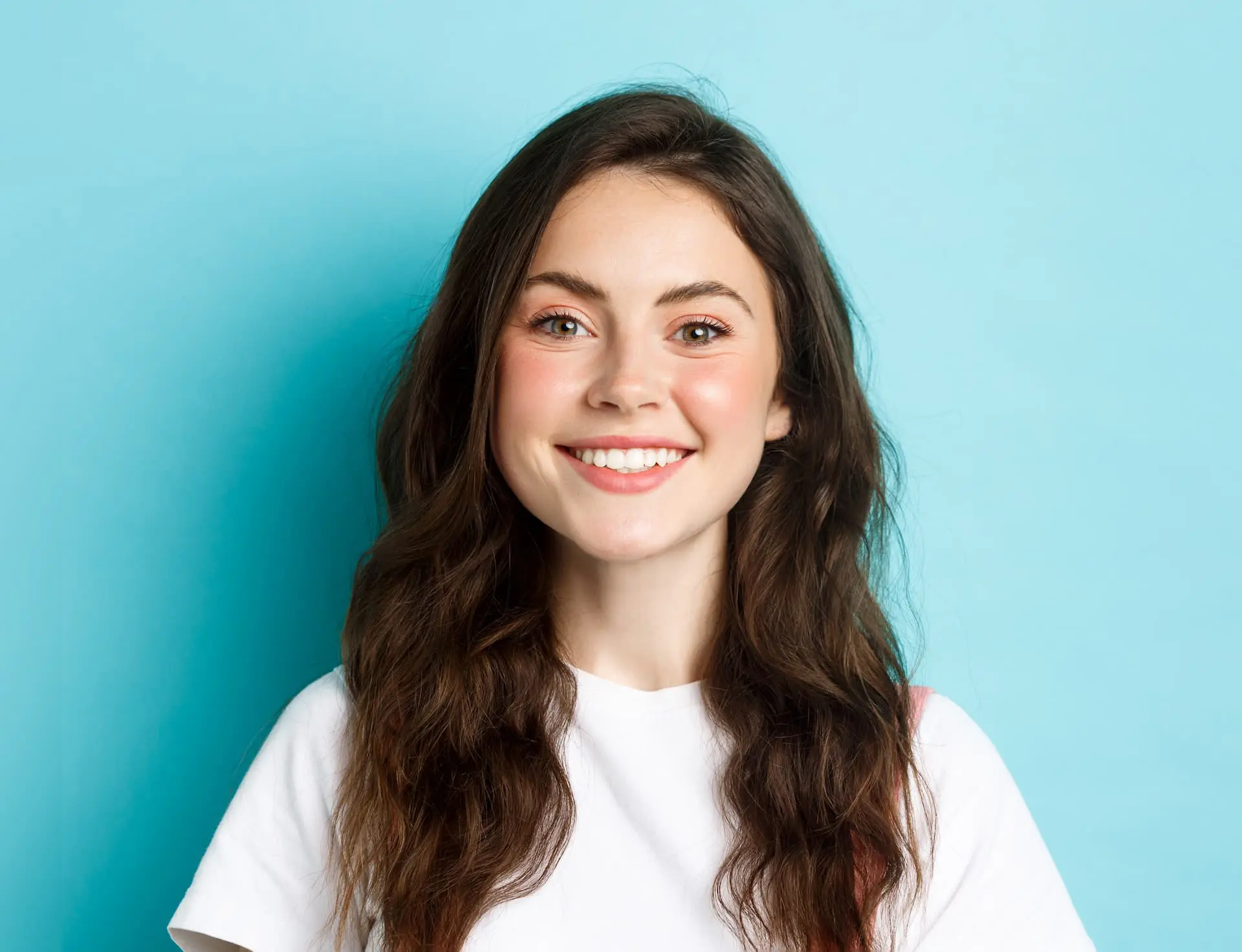 Showcase your confident smile after getting affordable braces at Levine Orthodontics in Fort Myers, Cape Coral, or Lehigh Acres, FL—just like this young woman with long brown hair and a white t-shirt, beaming against a light blue background.