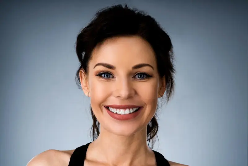 A woman with dark hair and blue eyes confidently smiles, displaying her ceramic braces in a photo for Levine Orthodontics in Fort Myers, Cape Coral, or Lehigh Acres, FL.