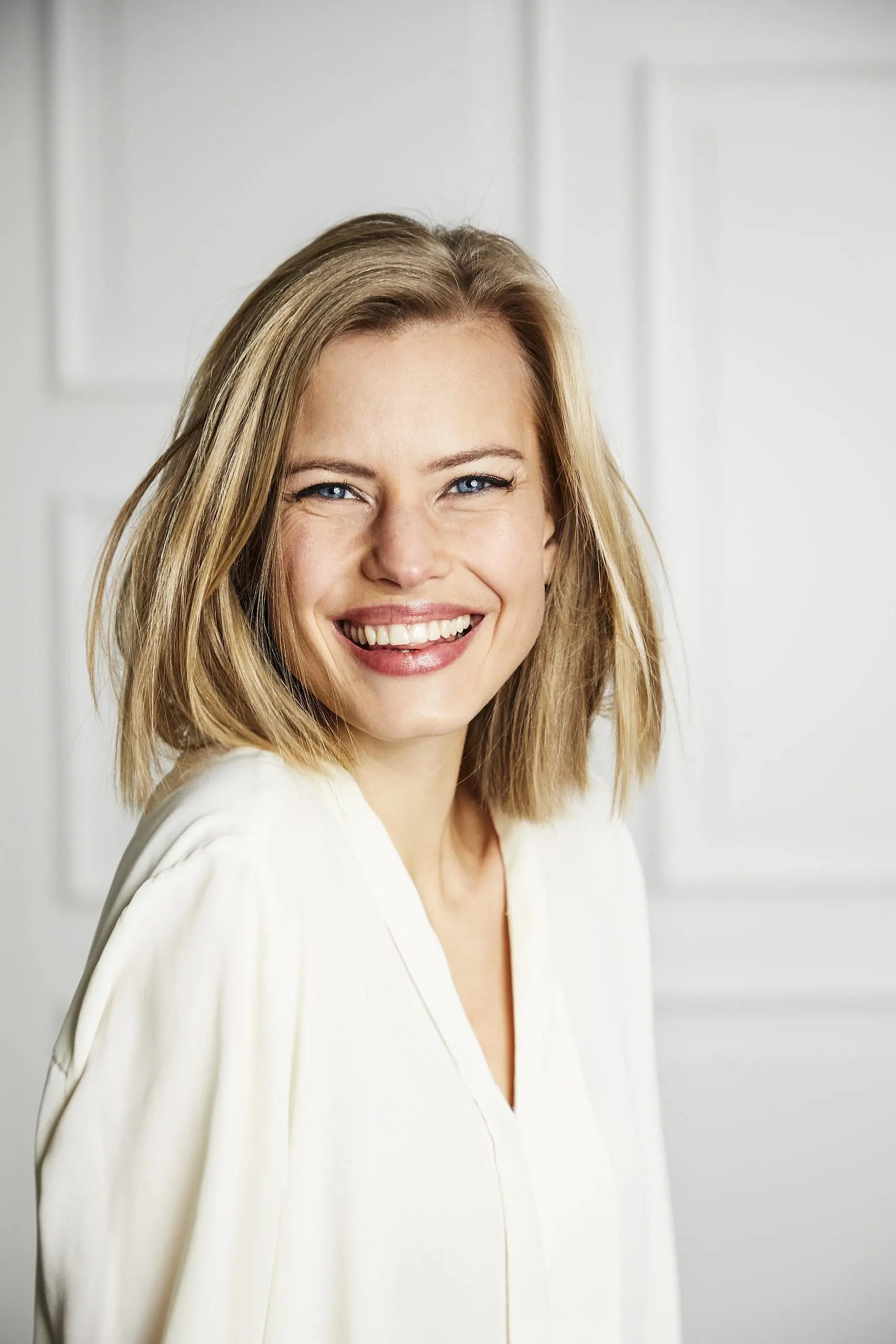 Confident in her smile thanks to an Invisalign Payment Plan from Levine Orthodontics in Fort Myers, Cape Coral, or Lehigh Acres, FL, a blonde woman in a white blouse smiles at the camera against a plain light background.