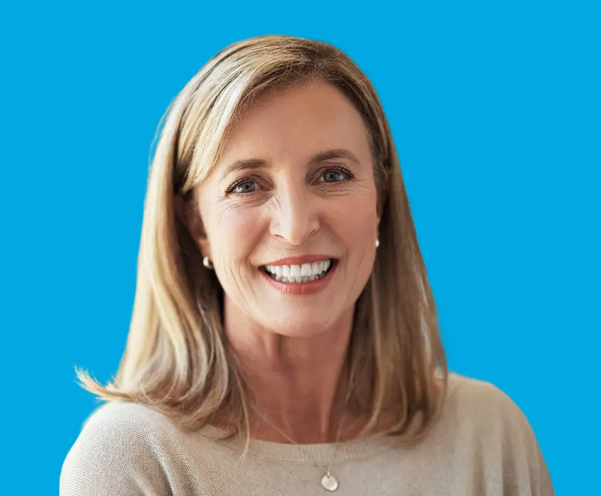 A woman with light brown hair and a beige sweater smiles at the camera against a solid blue background, representing Levine Orthodontics in Lehigh Acres, FL.