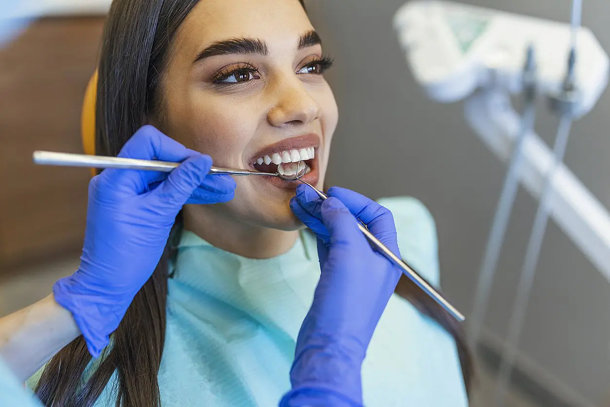 At Levine Orthodontics in Fort Myers, Cape Coral or Lehigh Acres, FL, a dentist in blue gloves examines a smiling woman's teeth while discussing affordable Invisalign options for a straighter smile.