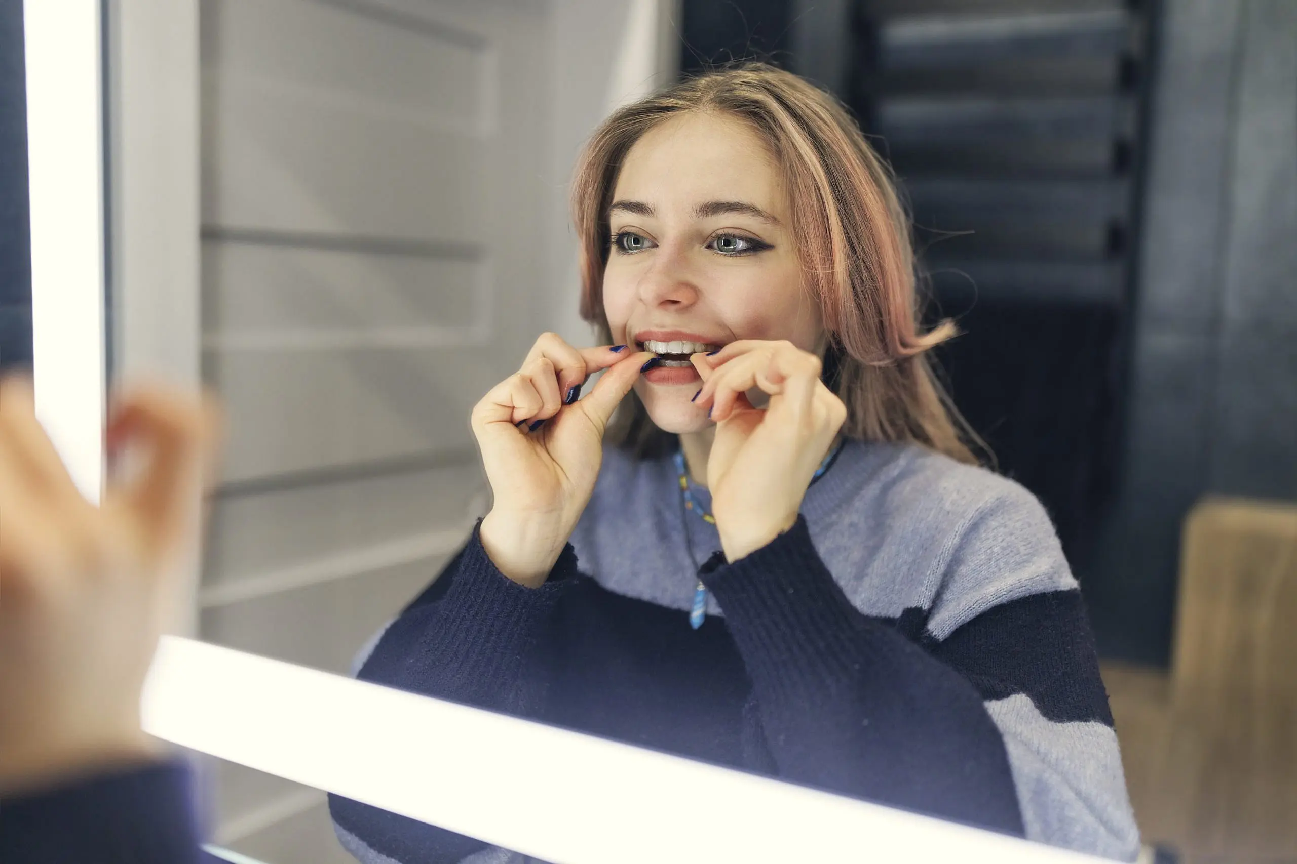 After Affordable Invisalign treatment at Levine Orthodontics in Fort Myers, Cape Coral, or Lehigh Acres, FL, a woman uses dental floss in front of a mirror to maintain her smile.