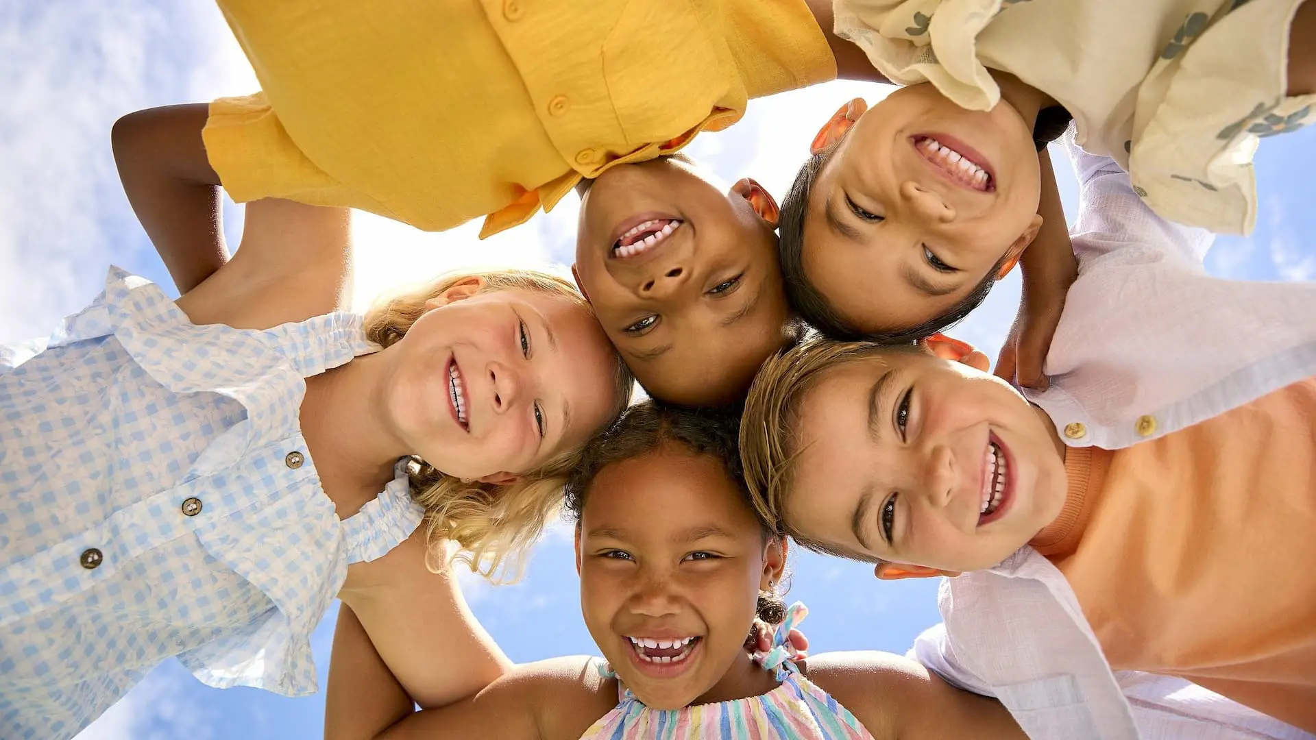 A group of five children stands outdoors in a circle, smiling down at the camera under a blue sky—a scene you might see near Levine Orthodontics in Fort Myers, Cape Coral, or Lehigh Acres, FL.