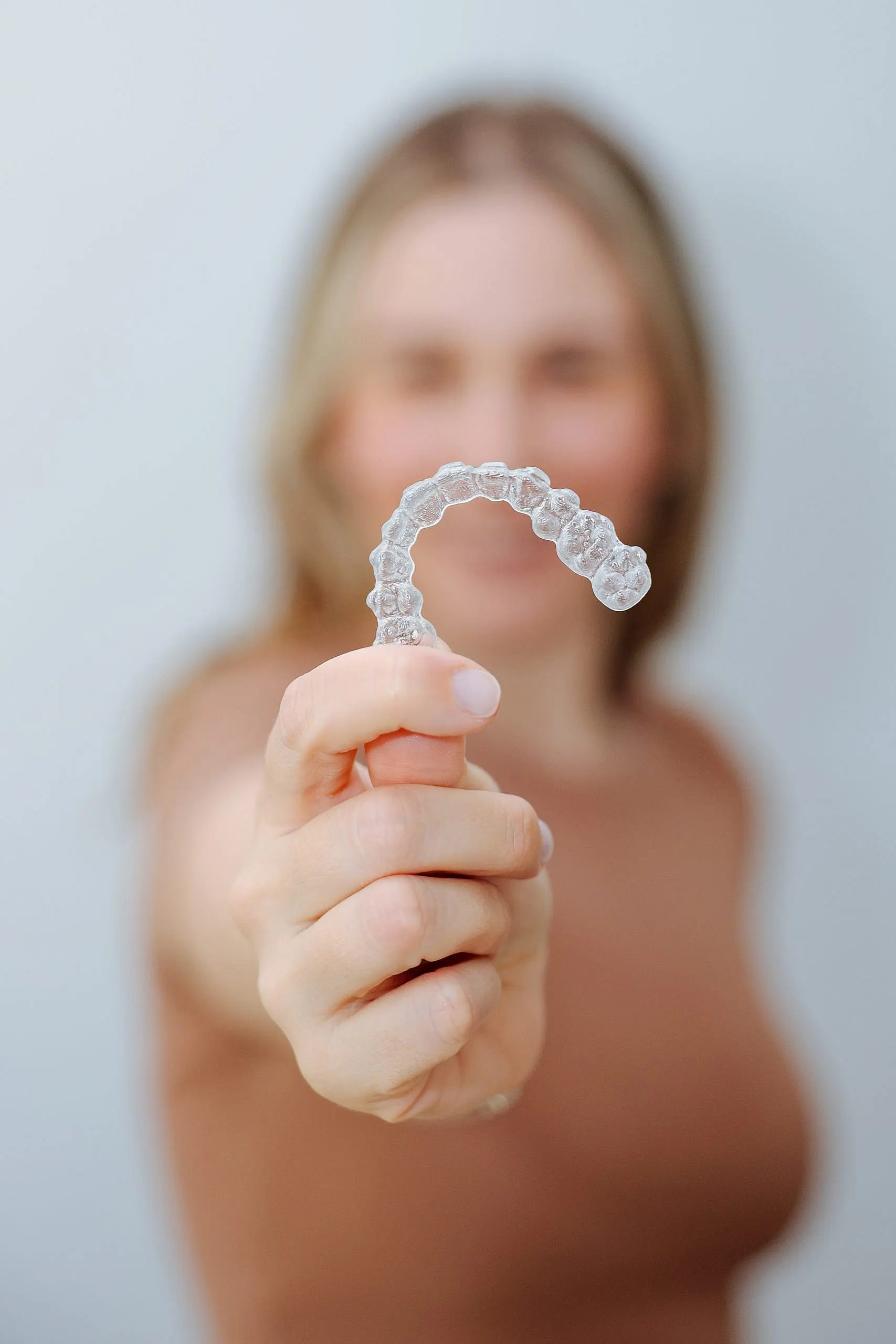 Highlighting the benefits of Invisalign insurance for orthodontic treatments, this image shows a person holding a clear dental aligner, with their face out of focus in the background perfect for patients considering Levine Orthodontics in Fort Myers, Cape Coral, or Lehigh Acres, FL.