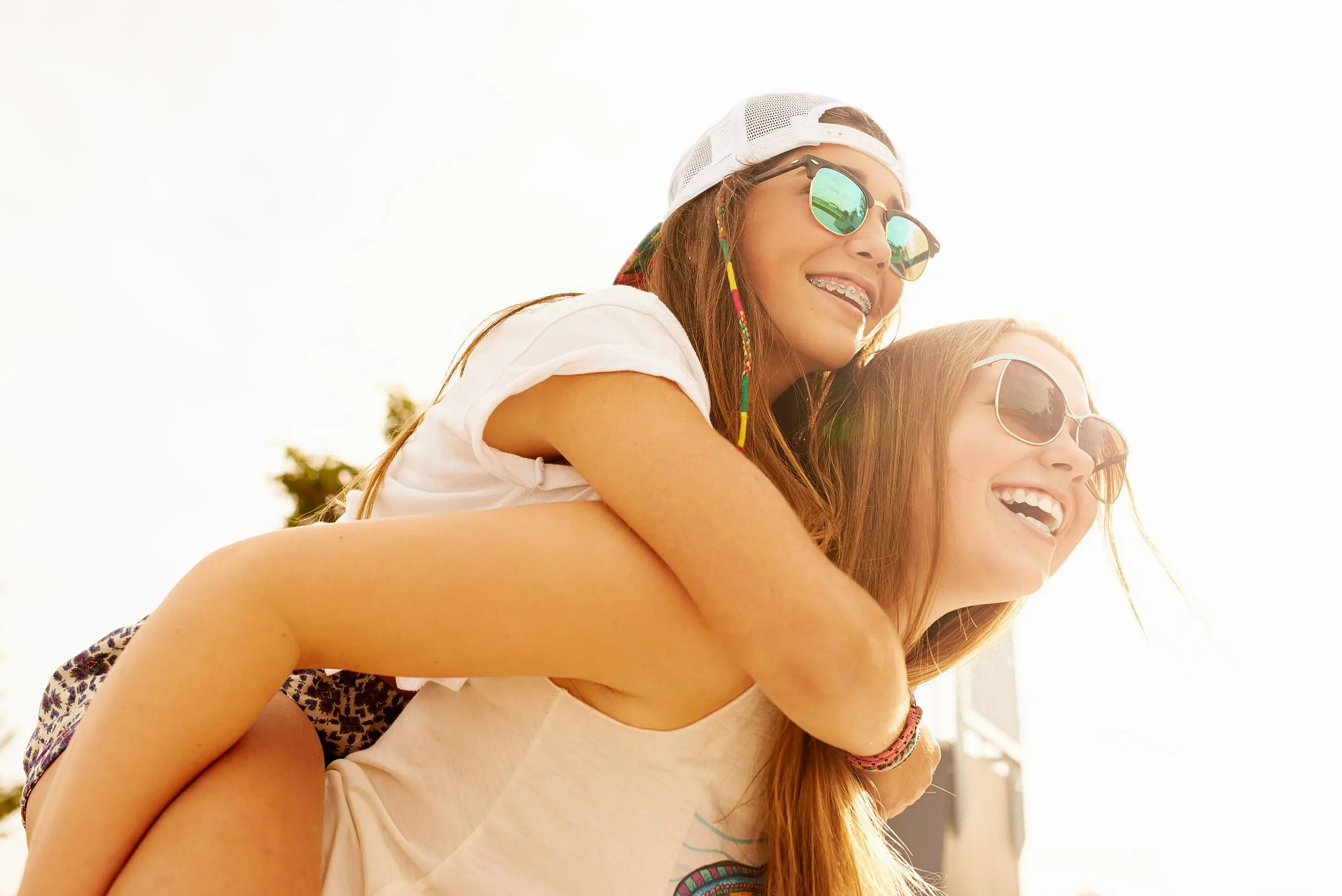 Enjoy carefree moments with a flexible Braces Payment Plan at Levine Orthodontics in Fort Myers, Cape Coral, or Lehigh Acres, FL—like these two young women outdoors, one giving the other a piggyback ride and flashing her braces with a smile.