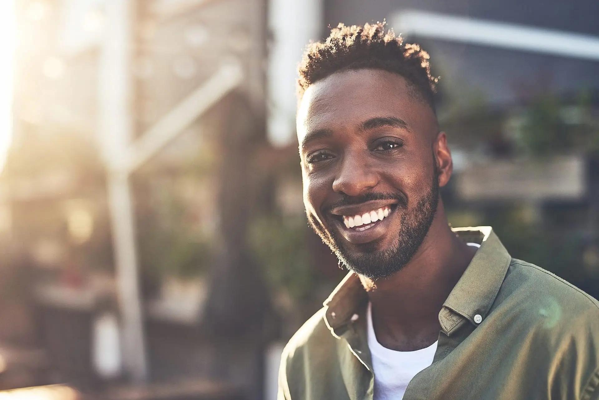 Radiating confidence outdoors in the sunlight, a man with short curly hair and a beard smiles in his green shirt—much like someone who discovered their perfect Invisalign Payment Plan at Levine Orthodontics in Fort Myers, Cape Coral, or Lehigh Acres, FL.