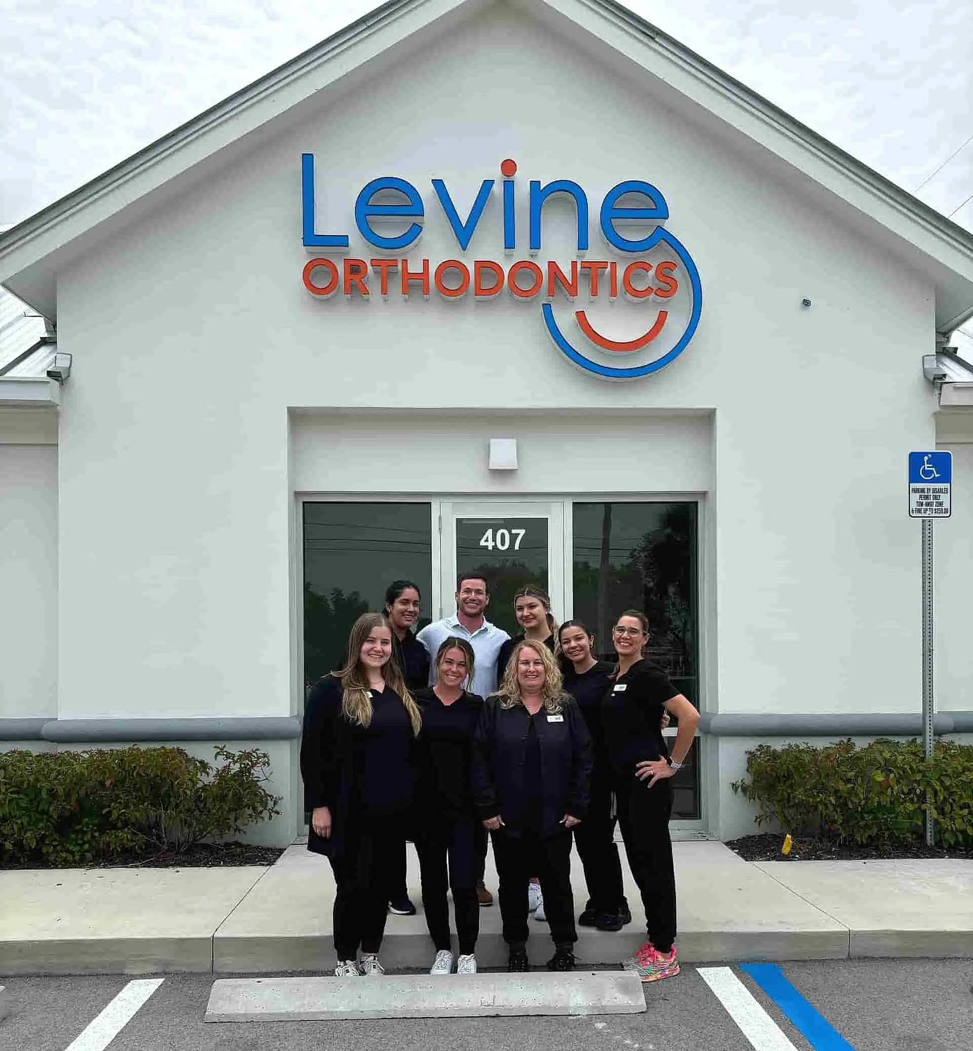 A group of seven, including Dr. Alex Levine, poses for a photo in front of the Levine Orthodontics building under the sign, located in Fort Myers, Cape Coral or Lehigh Acres, FL.