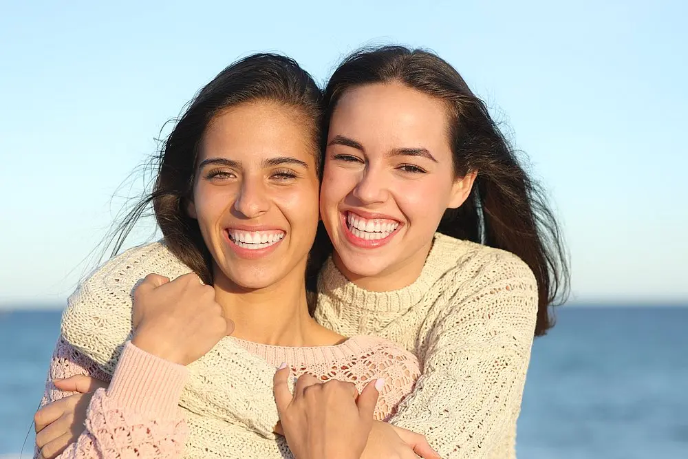 Enjoying the sunshine, two young women share a joyful smile and hug on a scenic beach—capturing the happiness that comes with confident smiles from Levine Orthodontics in Fort Myers, Cape Coral or Lehigh Acres, FL.