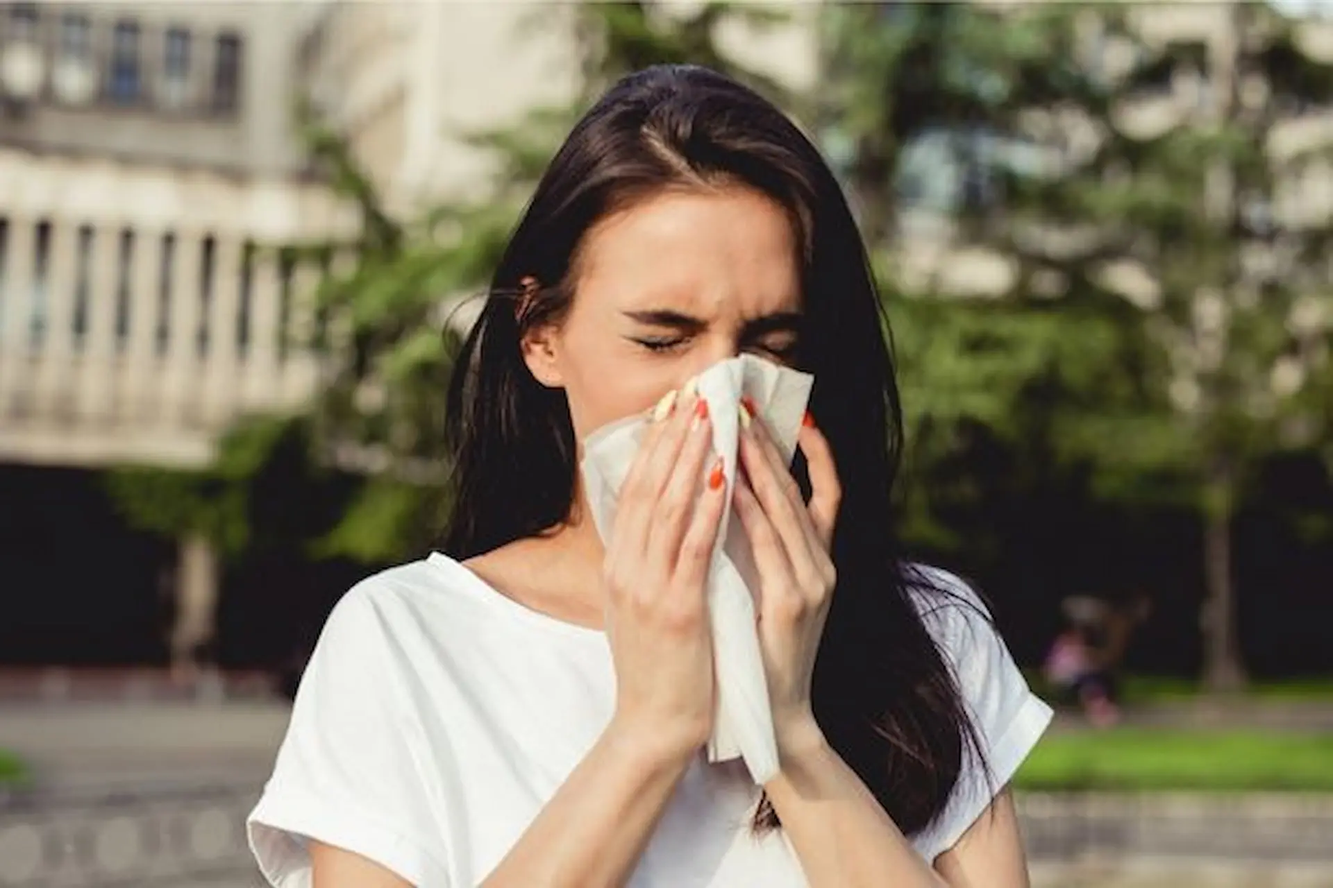 Sneezing into her hands, a woman in a white shirt stands outside, reminiscent of the dedicated mouth breather one might encounter at Levine Orthodontics in Fort Myers, Cape Coral or Lehigh Acres, FL.