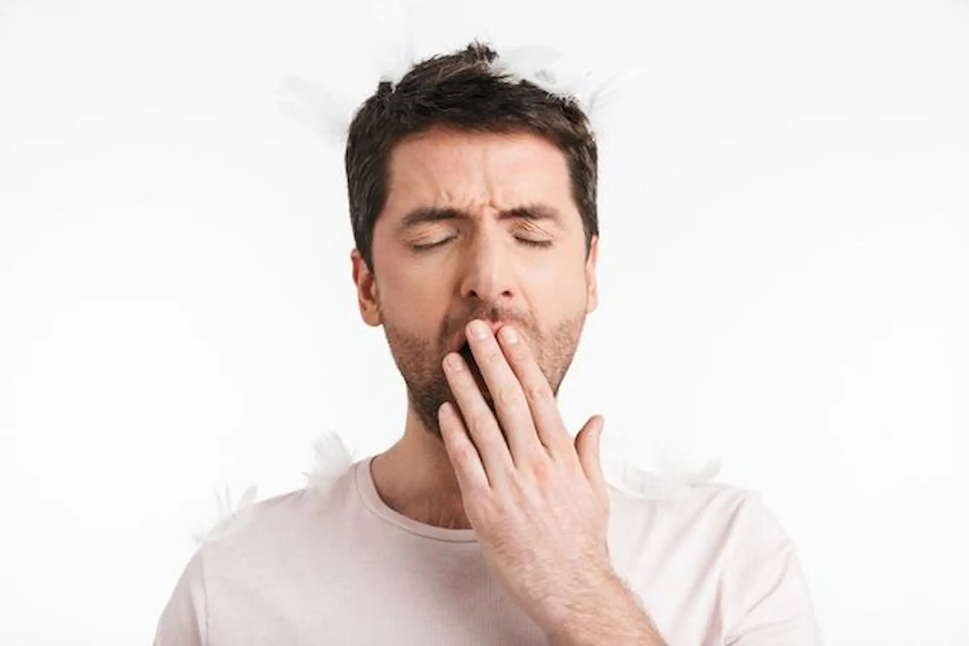 A man, possibly a mouth breather, yawns with his hands over his mouth in a white shirt. To address potential breathing issues, Levine Orthodontics in Fort Myers, Cape Coral or Lehigh Acres, FL might offer suitable solutions.