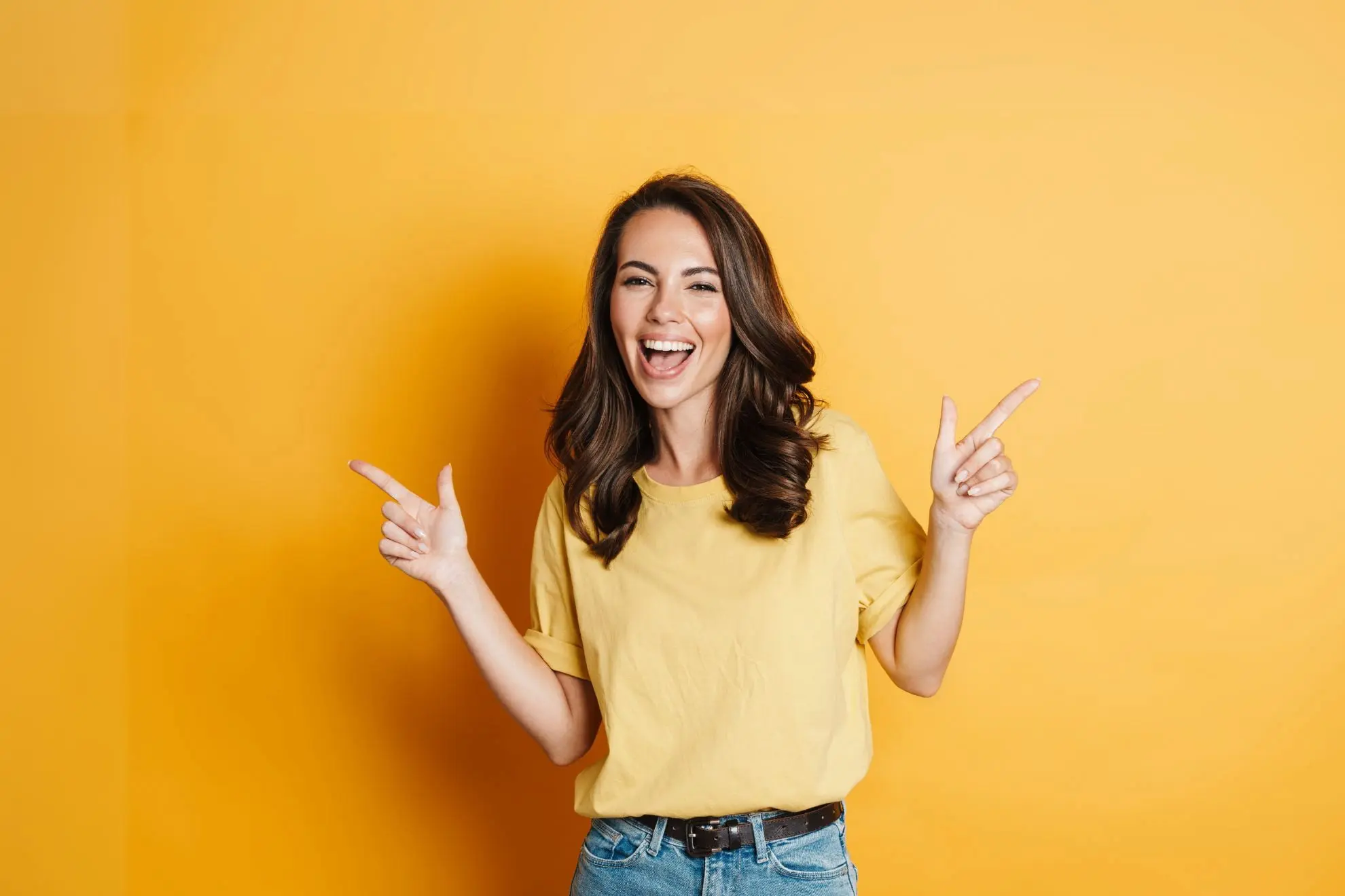 At Levine Orthodontics in Fort Myers, Cape Coral, or Lehigh Acres, FL, a woman with long dark hair smiles and points to her teeth, highlighting her happiness—possibly celebrating her new smile after learning about the cost of Invisalign clear aligners.