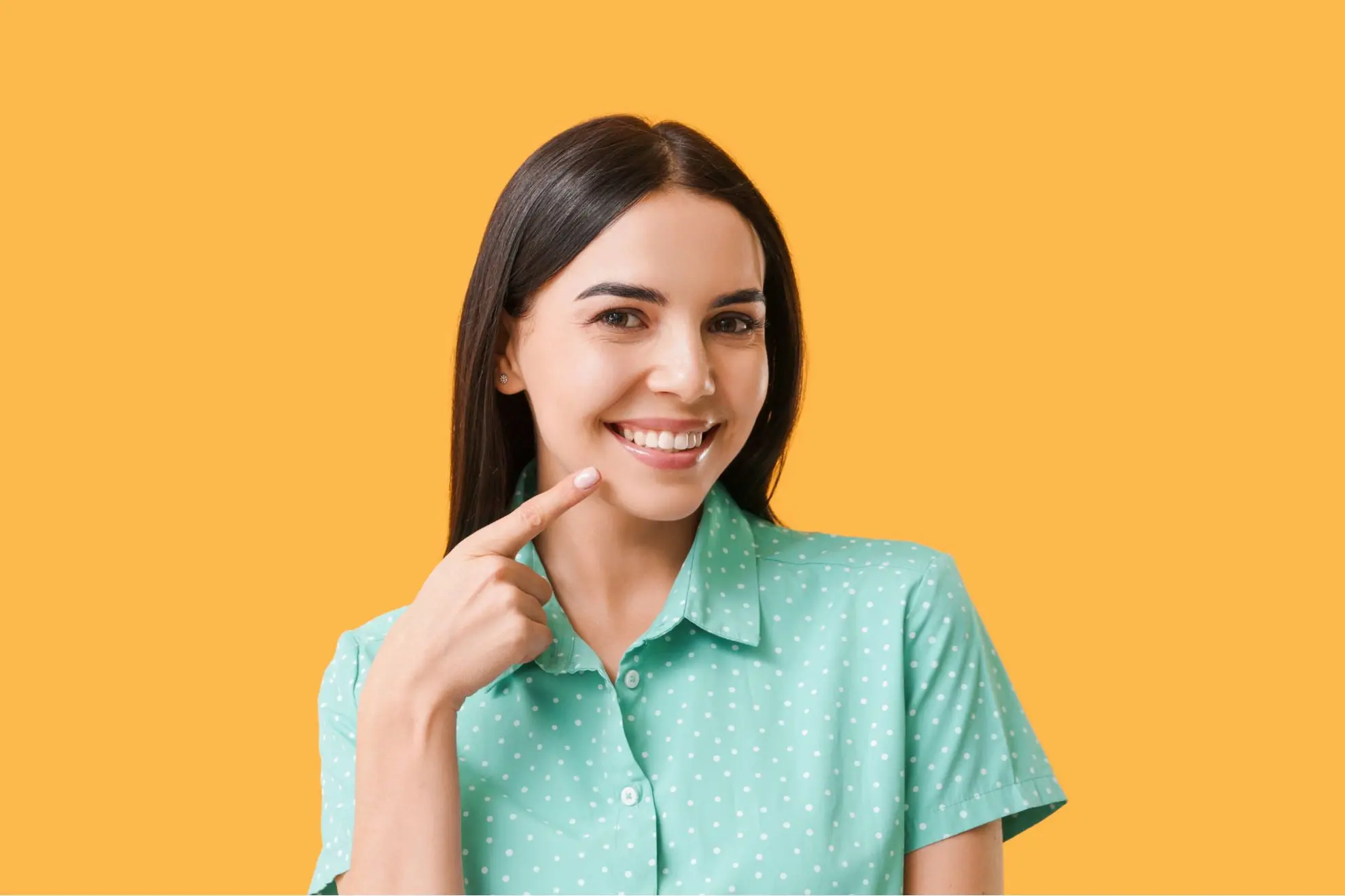 At Levine Orthodontics in Fort Myers, Cape Coral, or Lehigh Acres, FL, a woman with long dark hair smiles and points to her teeth, highlighting her happiness—possibly celebrating her new smile after learning about the cost of Invisalign clear aligners.
