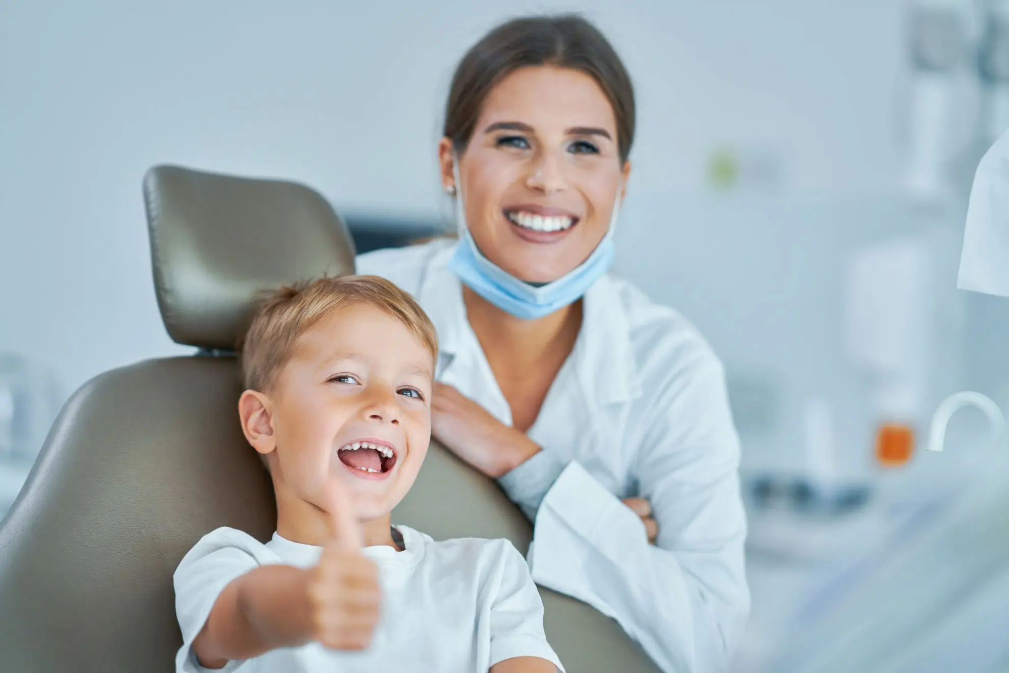 Smiling child sitting in the dentist chair giving a thumbs up after a tongue thrust exam, with the dentist smiling behind them at Levine Orthodontics in Fort Myers, Cape Coral, or Lehigh Acres, FL.