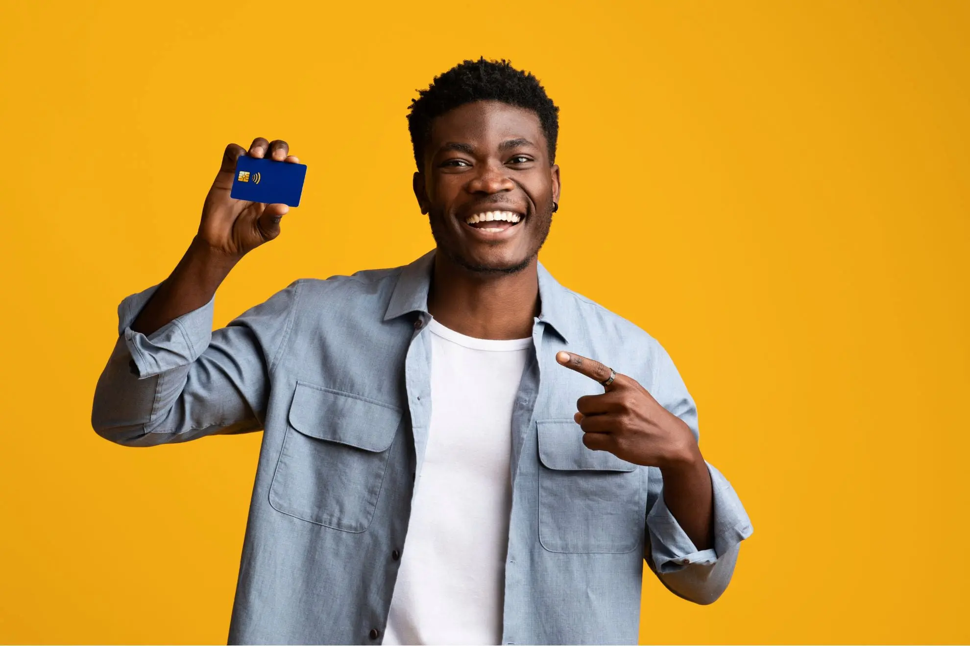 A smiling man in a light blue shirt points to a blue credit card against a yellow background, highlighting the affordable payment plan he received for his Invisalign clear aligner treatment at Levine Orthodontics in Fort Myers, Cape Coral, or Lehigh Acres, FL.