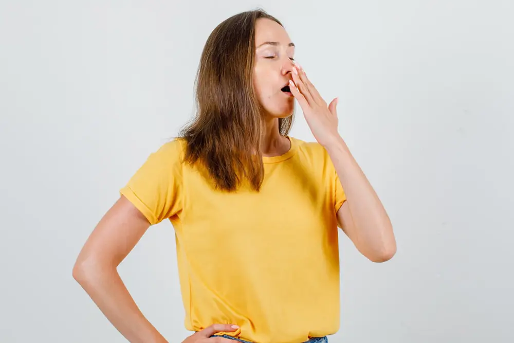 A woman in a yellow t-shirt yawns and covers her mouth, representing Airway Orthodontics at Levine Orthodontics in Fort Myers, Cape Coral, or Lehigh Acres, FL.