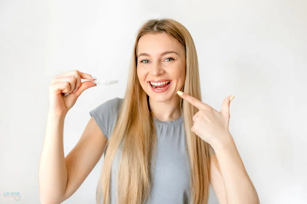 a woman pointing her teeth holding clear aligners - How Does Invisalign Work in Fort Myers, Cape Coral, and Lehigh Acres, FL 